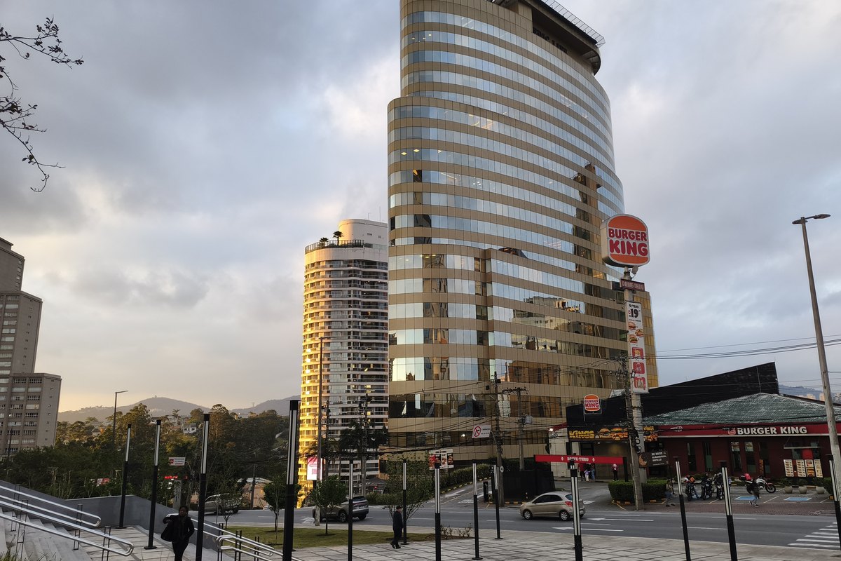 O edifício visto da esquina, com a travessia de pedestres e o comércio da avenida