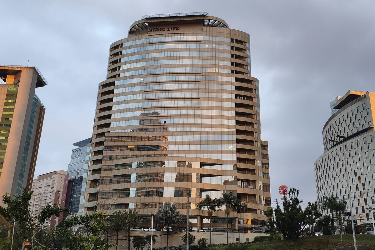Edifício comercial envidraçado onde fica a Clínica Gusman, visto da via de acesso